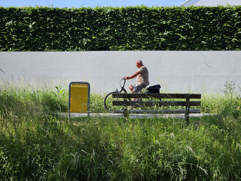 Man fietsend langs een bankje in het groen.